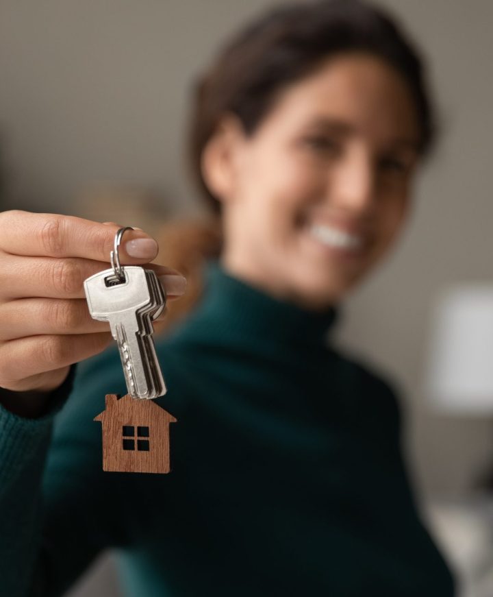 Close up focus on keys, smiling woman realtor selling apartment Close up focus on keys, smiling woman realtor selling apartment, offering to client, showing at camera, holding documents, contract, making purchasing deal, real estate agent, mortgage or rent